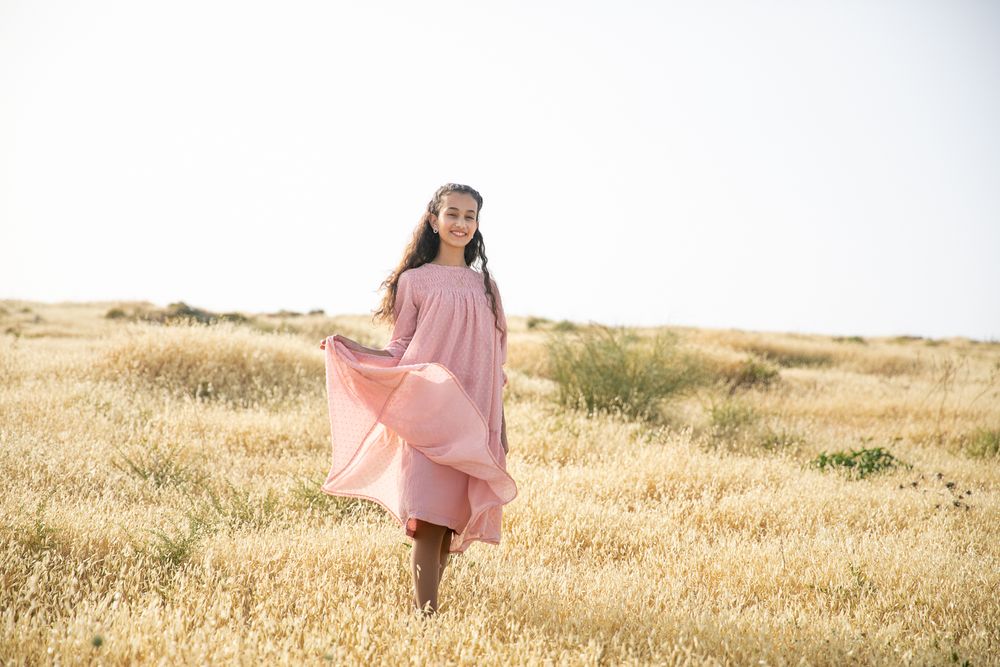 Portrait of a girl holding her dress and smiling in a golden field