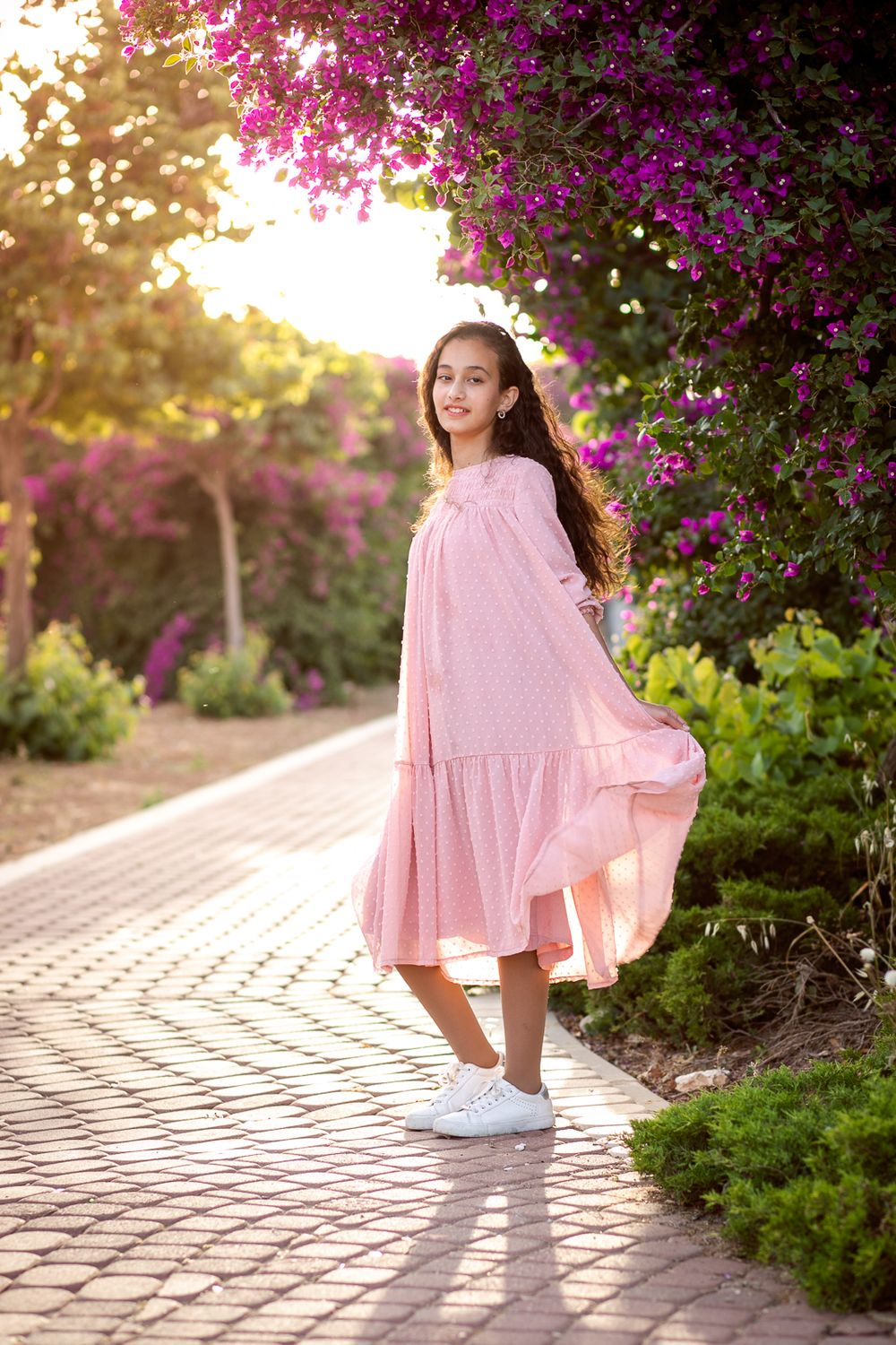 A girl stands by the flowers and holds her pink dress