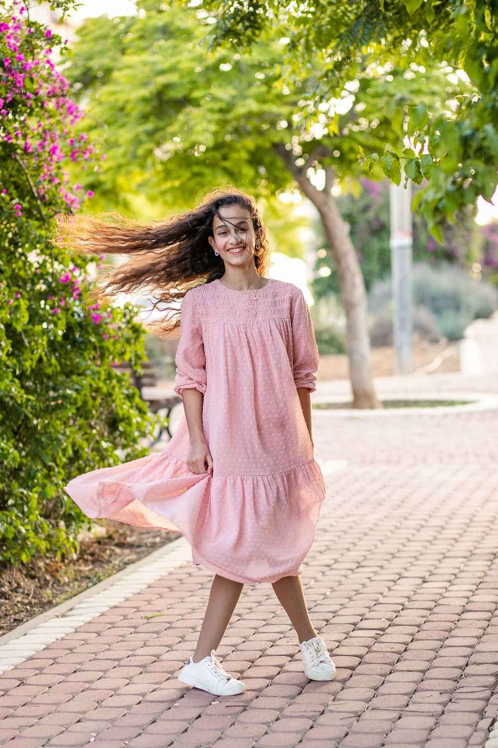 A girl in a pink dress dances next to the flowers