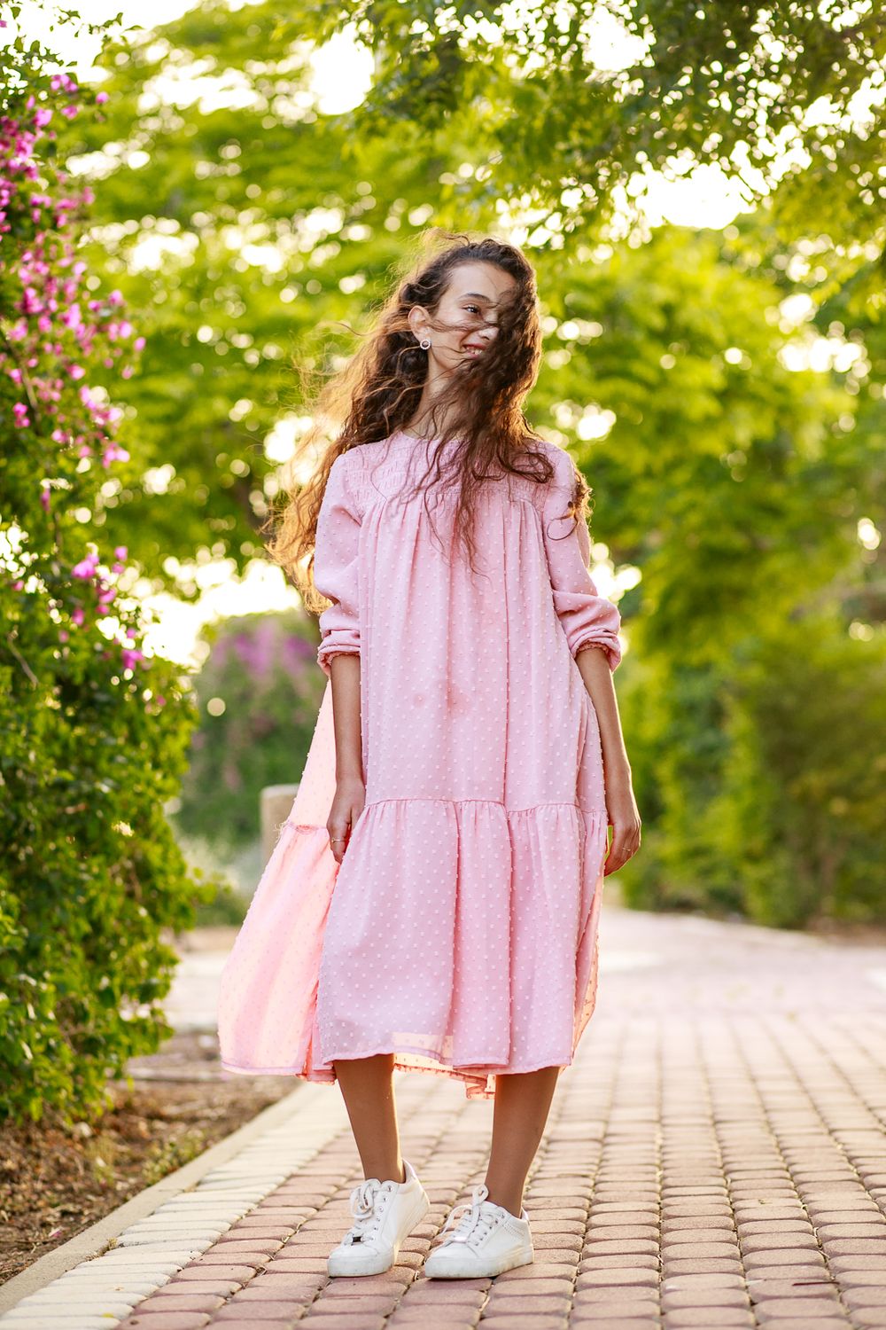 A girl in a pink dress stands next to the flowers