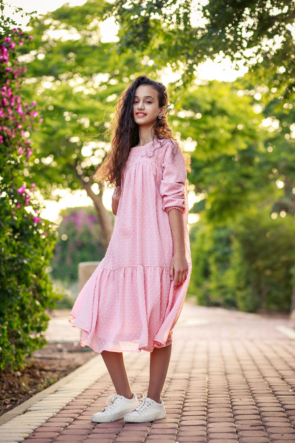 A girl in a pink dress stands next to the flowers