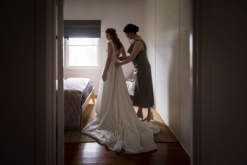 Bride with her Bridesmaid helping with her wedding dress before her wedding ceremony at St.Leonards Vineyard