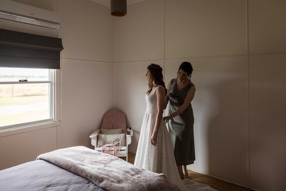 Bride with her Bridesmaid helping with her wedding dress before her wedding ceremony at St.Leonards Vineyard