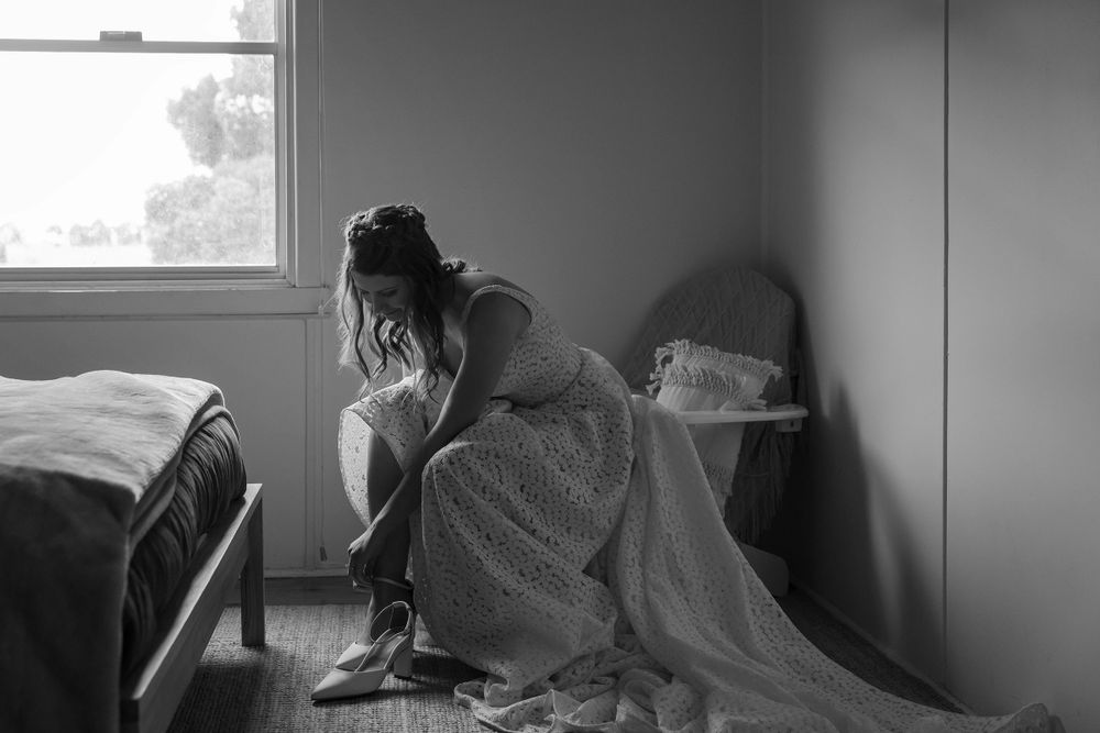 Bride in her wedding dress putting on her wedding shoes before her wedding ceremony at St.Leonards Vineyard