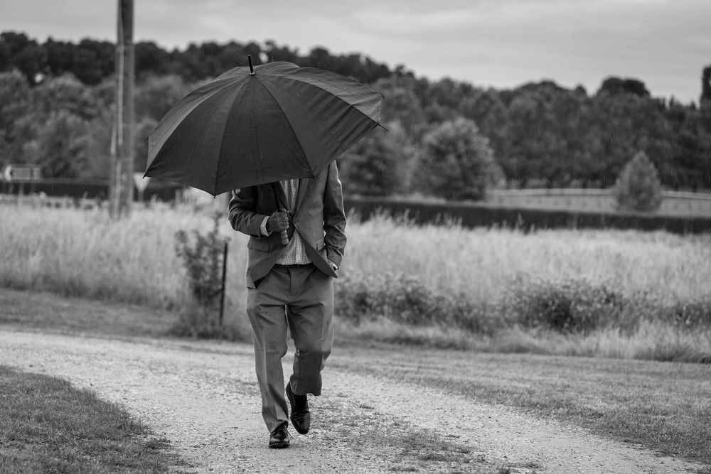 A black and white photo of someone walking with an umbrella on a rural path.
