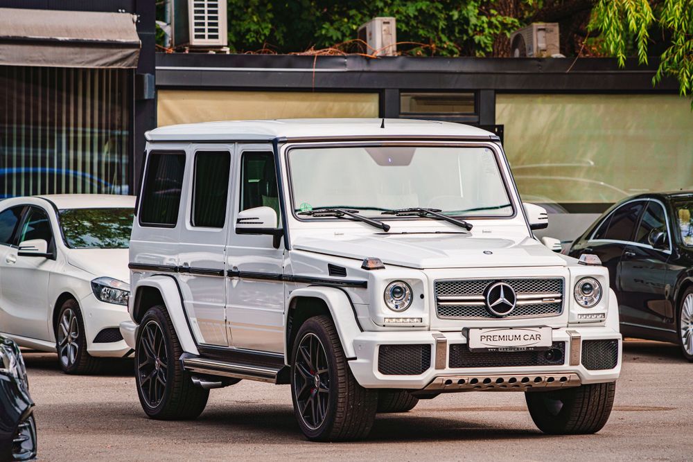 Side profile of a white Mercedes G-Class SUV parked among other luxury vehicles.