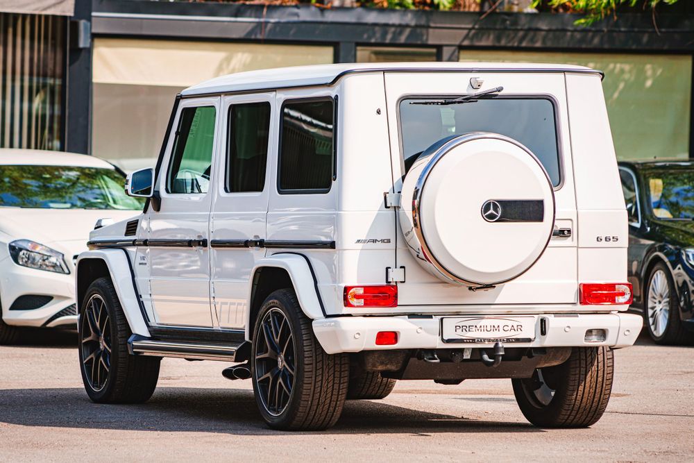 White Mercedes-Benz G-Class SUV with black wheels parked outside a premium dealership.