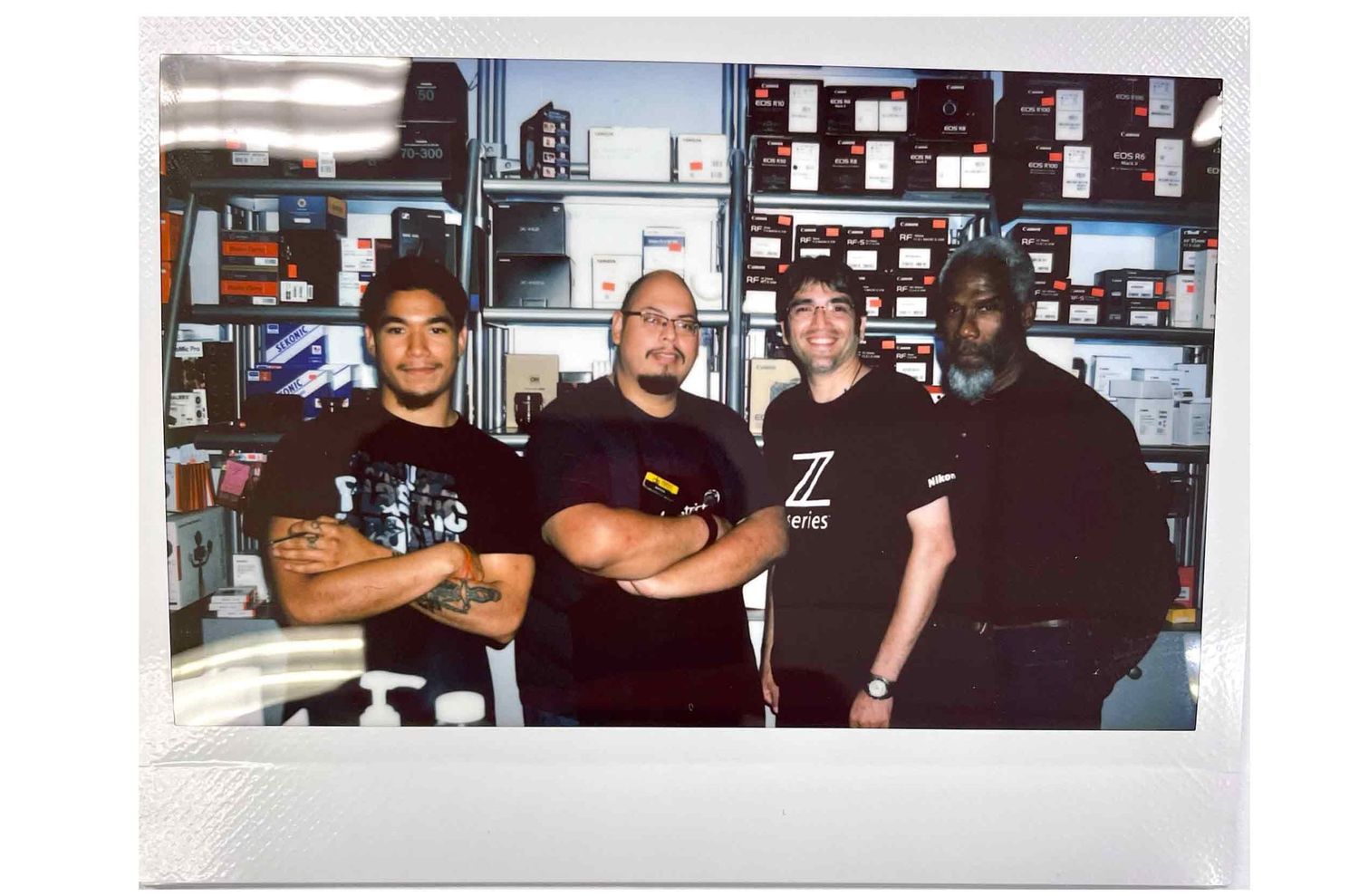 Four men posing together inside a store filled with shelves of products in an Instax instant photo.