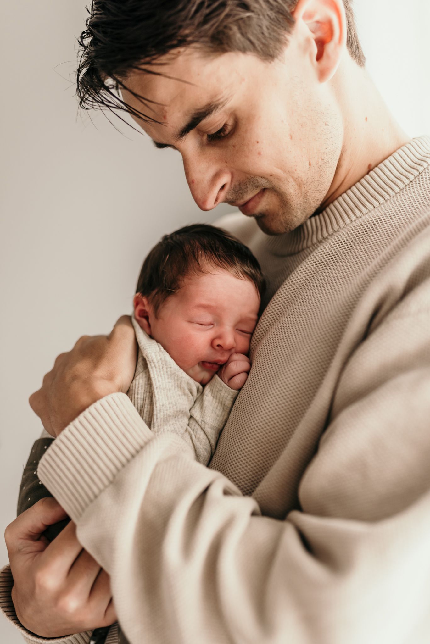 Tender moment of newborn baby sleeping peacefully against beige sweater.
