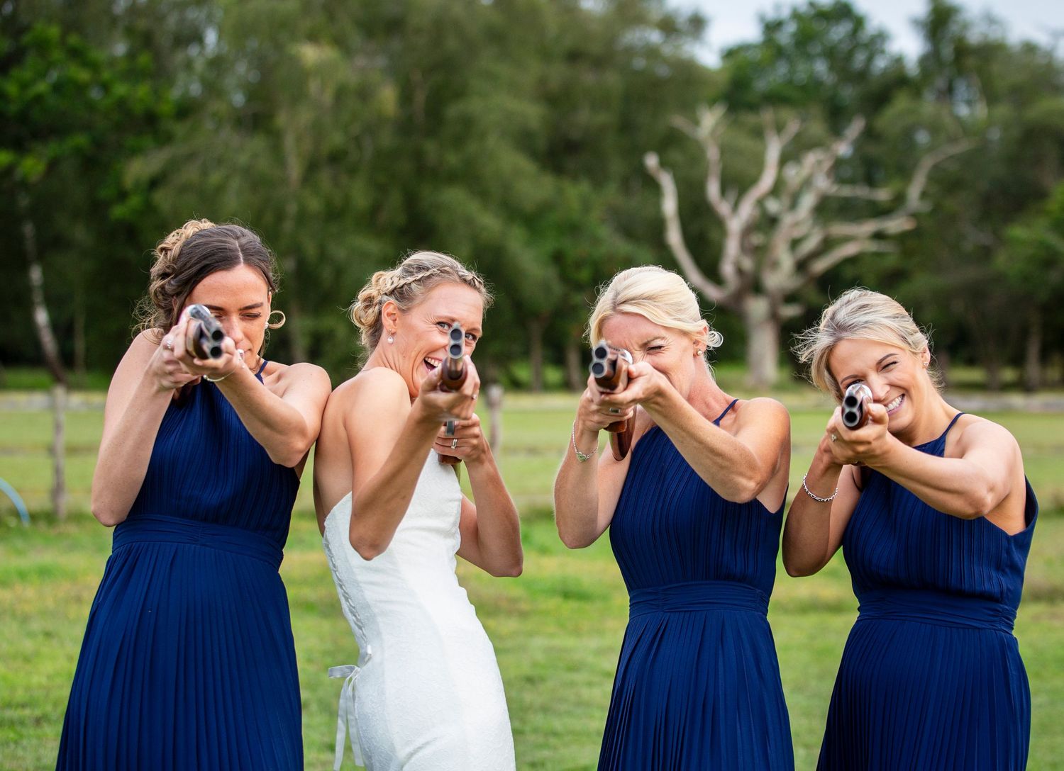 Wedding party in navy blue dresses poses playfully with the bride for a fun photo outdoors.