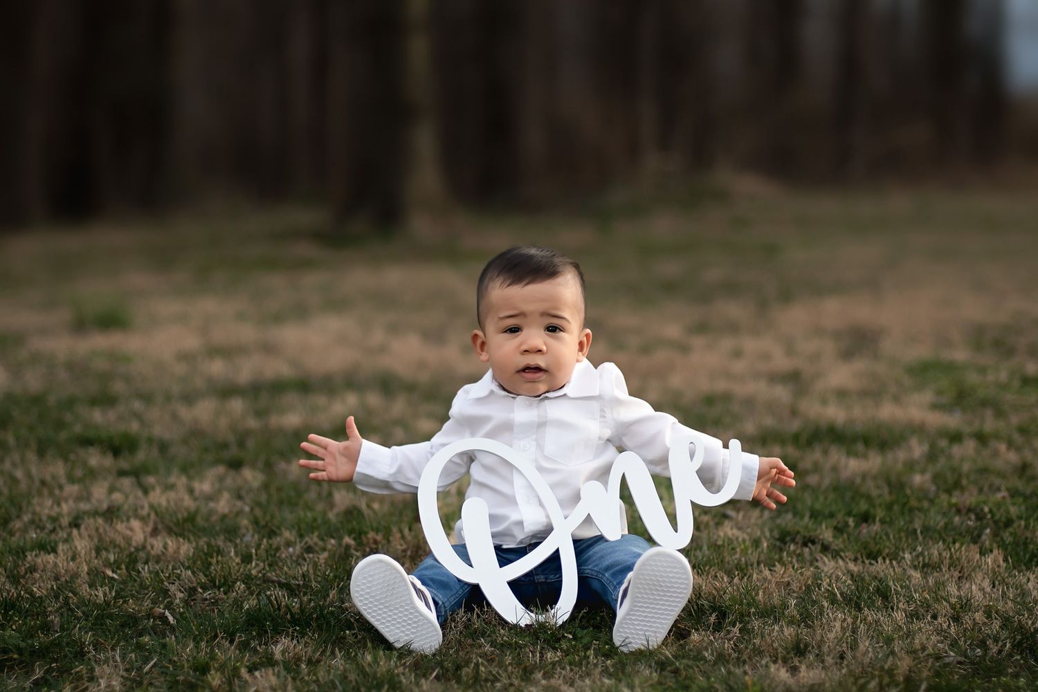 Baby dressed in white sitting on grass with decorative 'love' text overlay.