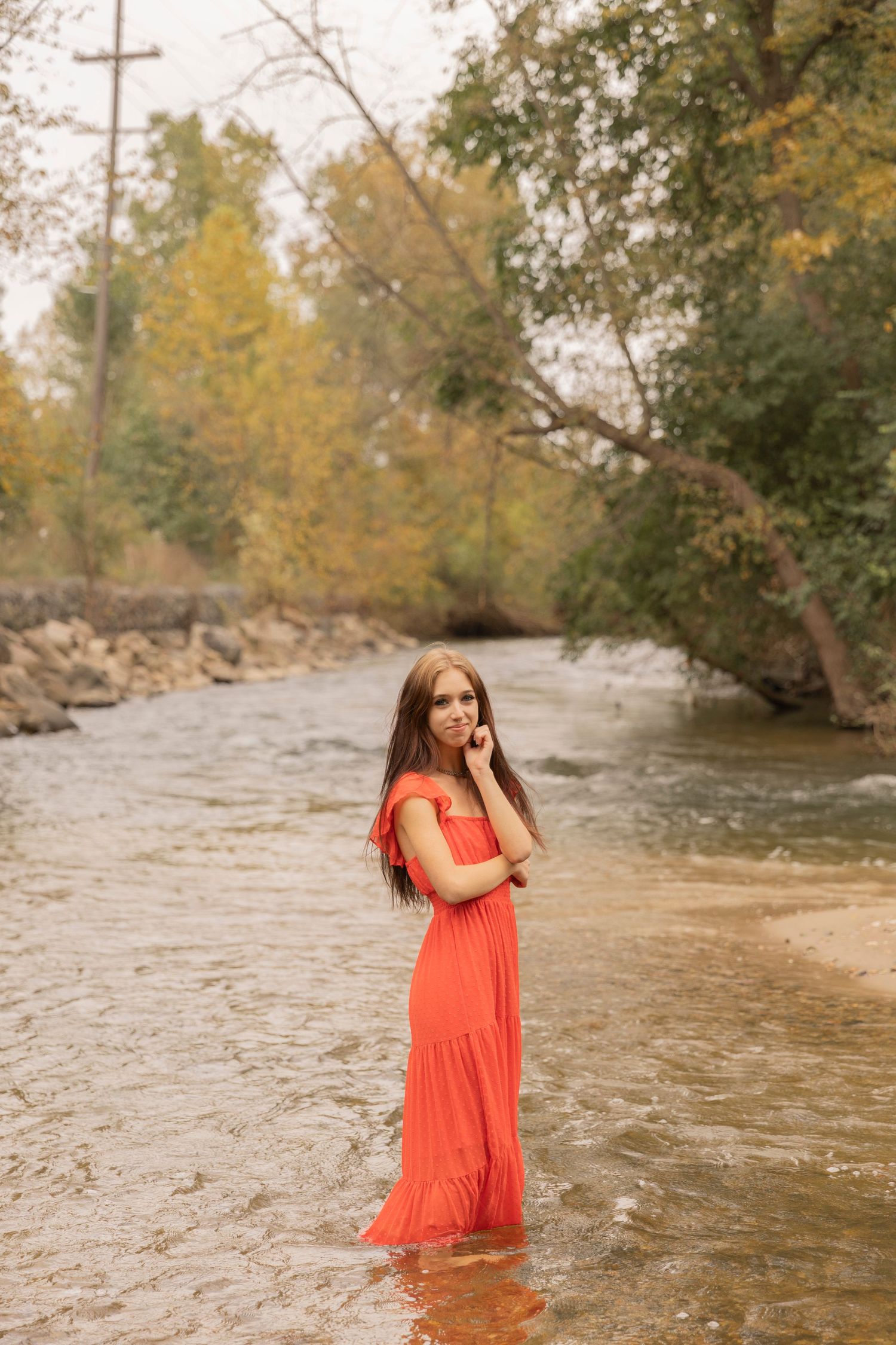 teenage girl in a orange dress standing in a creek in Rochester michigan
