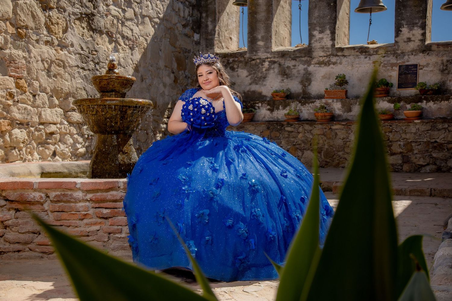 Young woman in a royal blue quinceañera ball gown poses at a historic stone mission.
