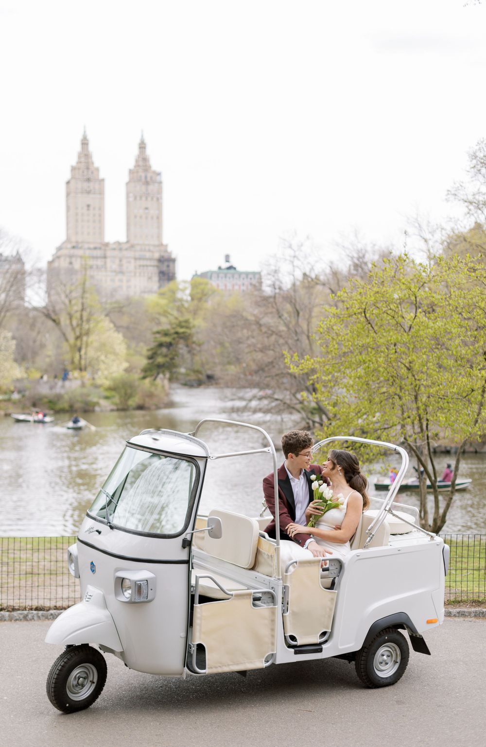 A couple sits in a white vintage cart with Central Park buildings visible in the background.