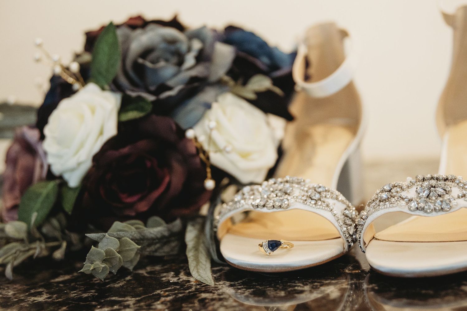 Wedding shoes and dark floral bouquet arrangement on textured surface.