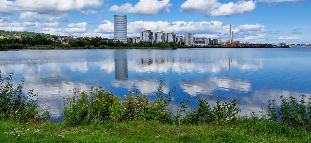 City skyline reflected in calm waters under blue sky with white clouds.