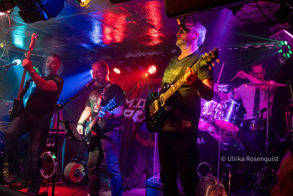 Musicians performing on stage under colorful lighting at a live concert venue.