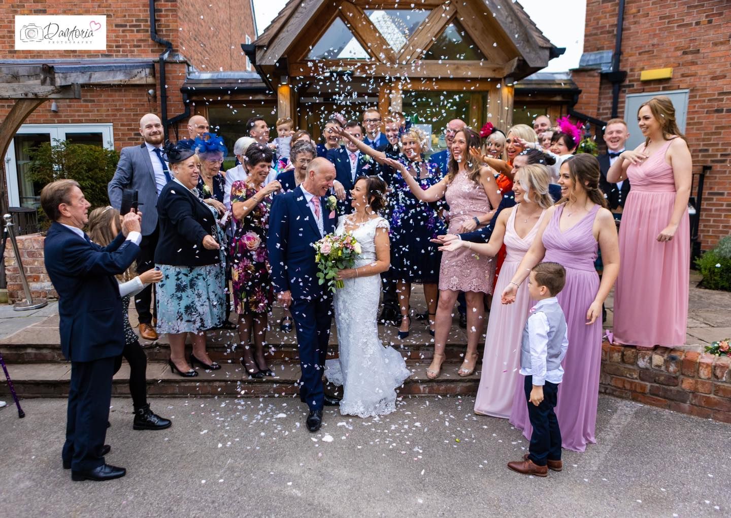 Wedding guests shower the couple with confetti outside a brick building during the celebration.