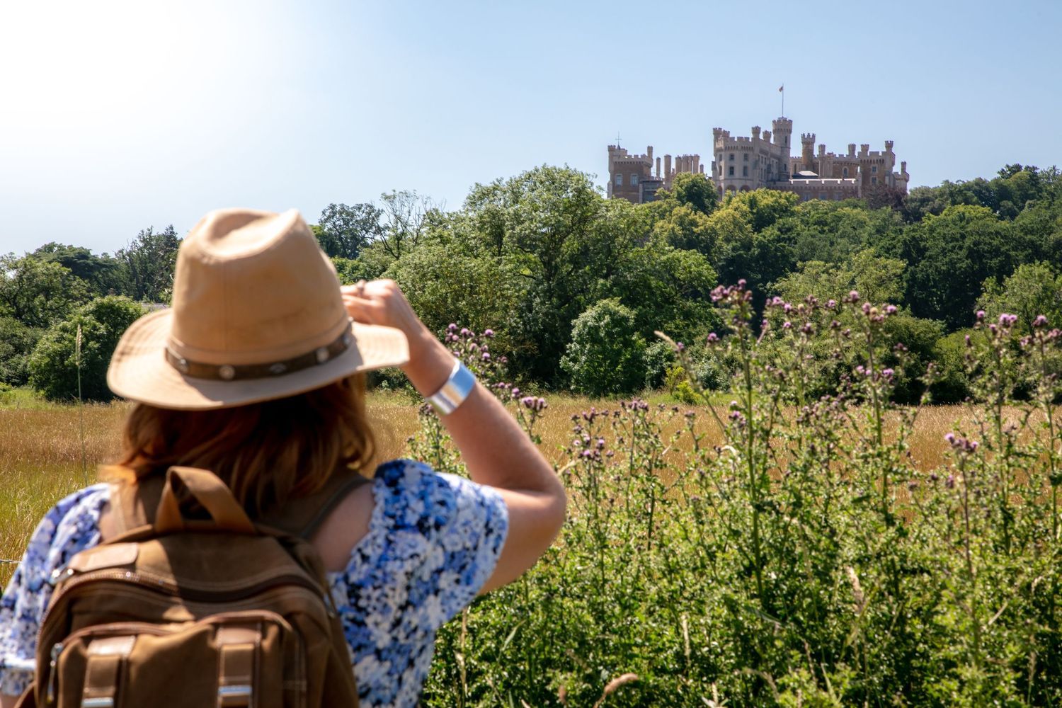 a woman in a fedora hat and rucksack looking towards Belvoir castle on the hill near grantham Lincolnshire