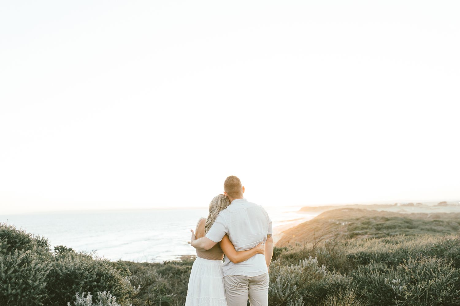 Couple sharing an intimate moment while overlooking coastal cliffs at sunset.