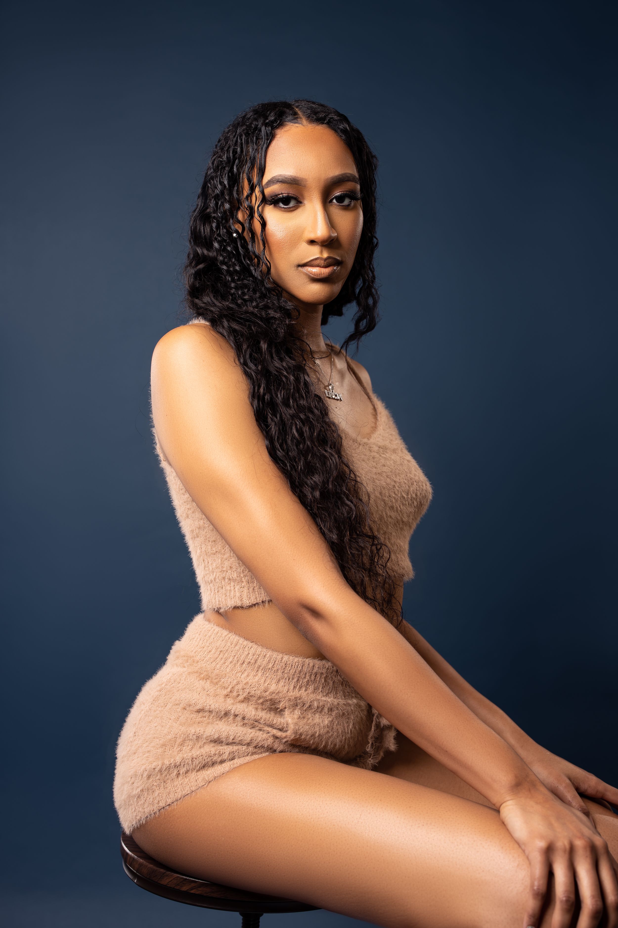 Studio portrait featuring a beige knit two-piece outfit against a dark blue background.