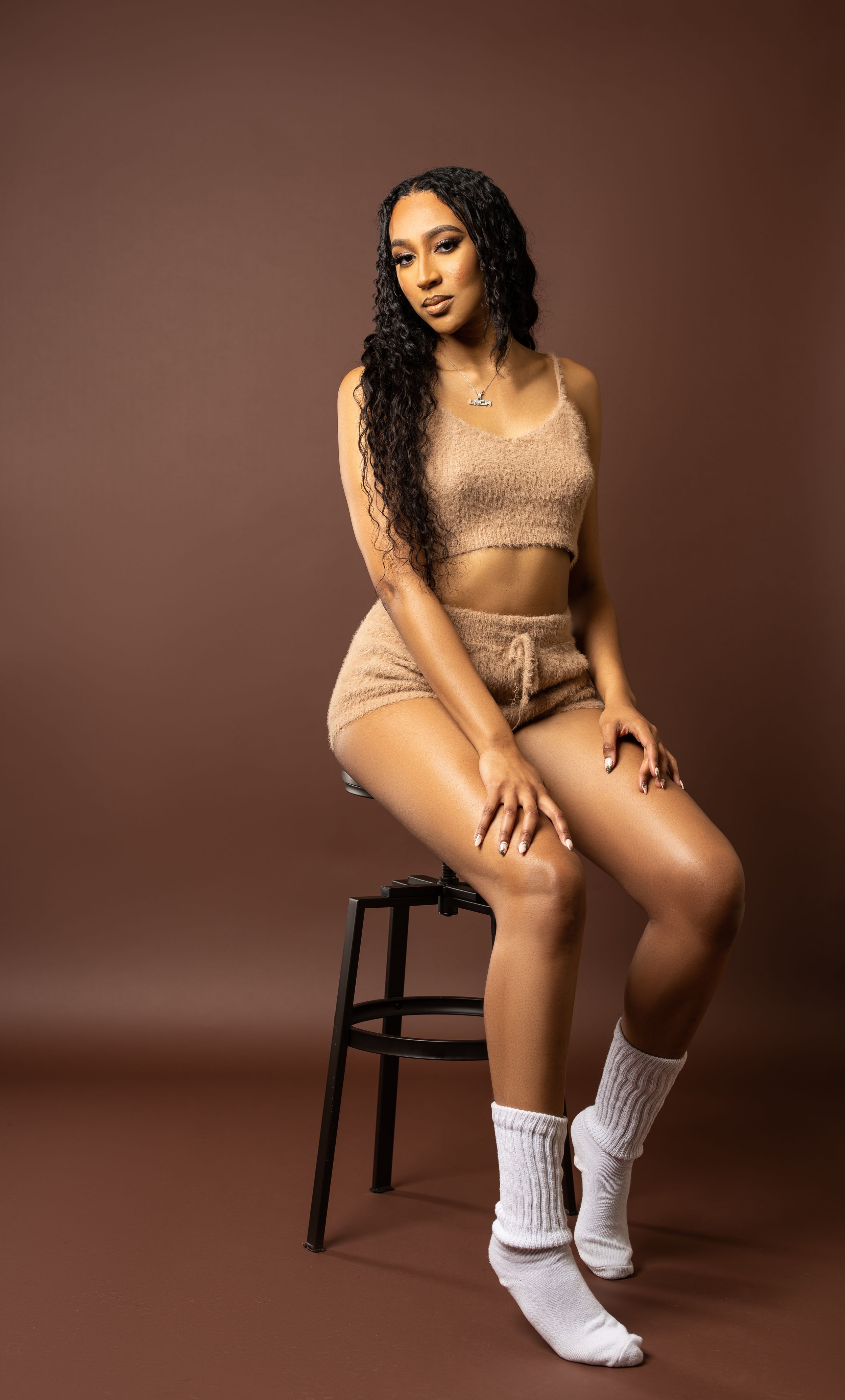 Lifestyle portrait in beige knit set posed on black stool.