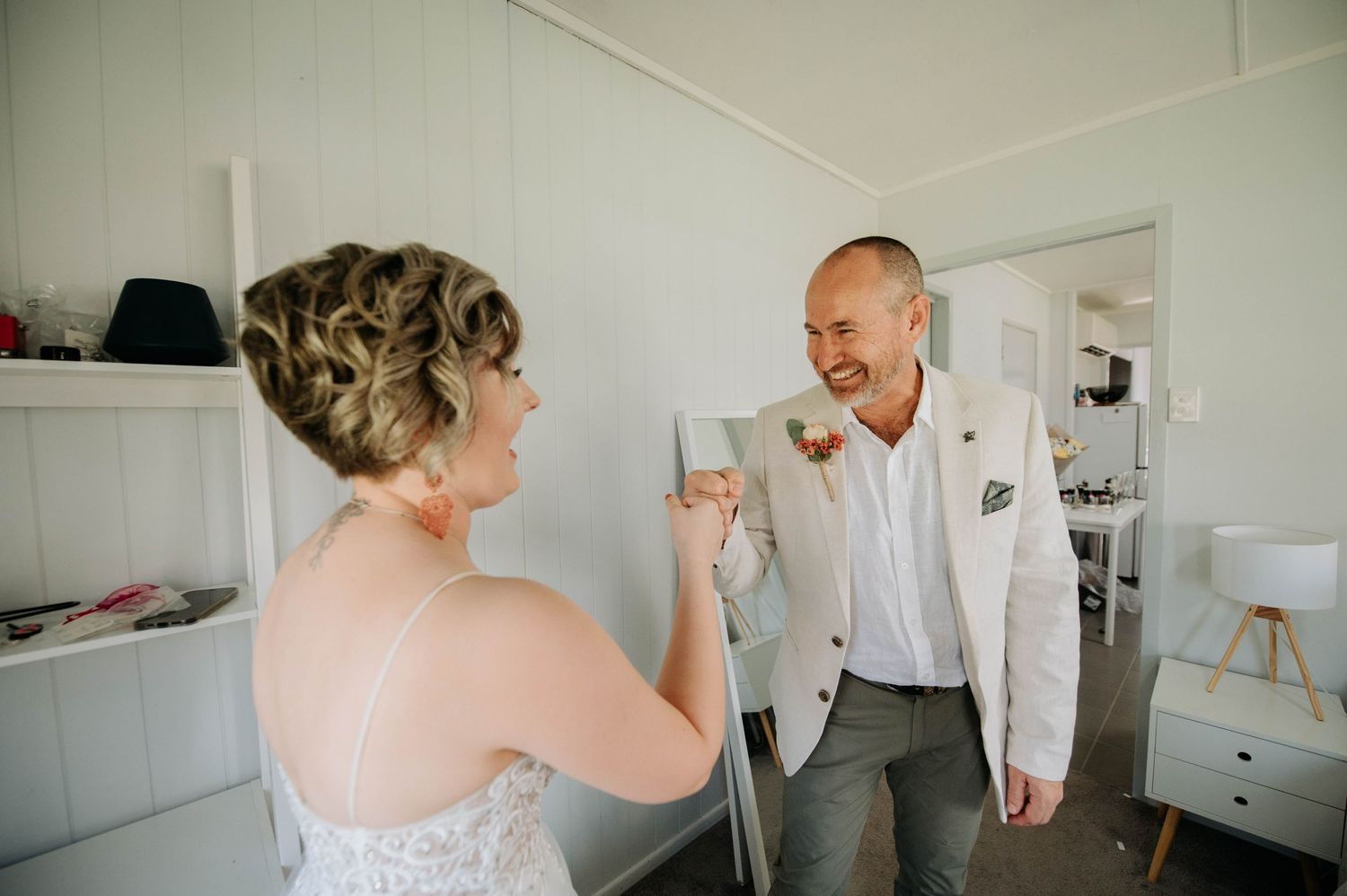 A wedding preparation moment captured between two people in a bright white room.