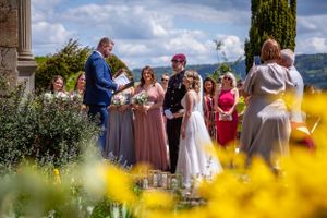 Outdoor wedding ceremony in bloom-filled garden with bridesmaids in pink dresses and military groom.