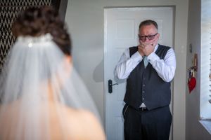 Emotional father covers his mouth in awe seeing his daughter in her wedding dress and veil for the first time.