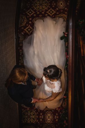 Aerial view of a bride in a flowing gown descending an ornate staircase with a companion beside her.