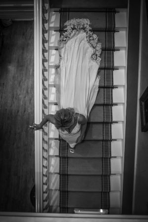 Black and white aerial view of a bride in a white gown descending a carpeted staircase.