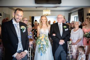 Bride walking down the aisle with her father beside the smiling groom during a wedding ceremony.