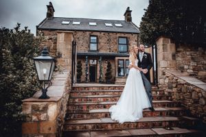 Bride and groom posing on stone steps in front of a beautiful rustic stone wedding venue.