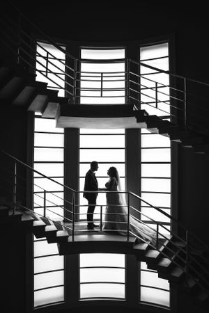 Dramatic black and white silhouette of bride and groom standing together in a modern spiral staircase.