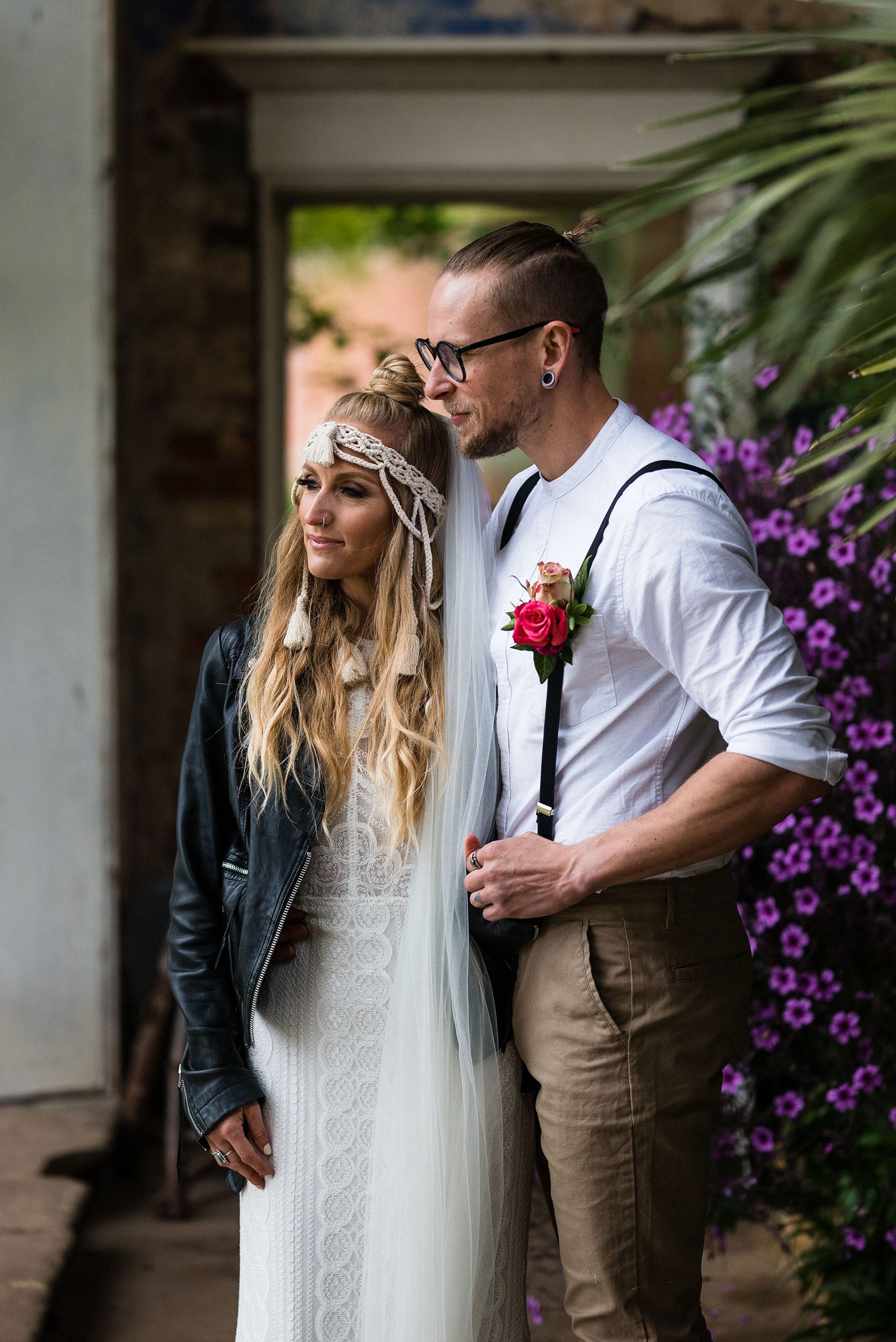 Wedding couple in relaxed alternative wedding outfits beside flowers at Calke Abbey