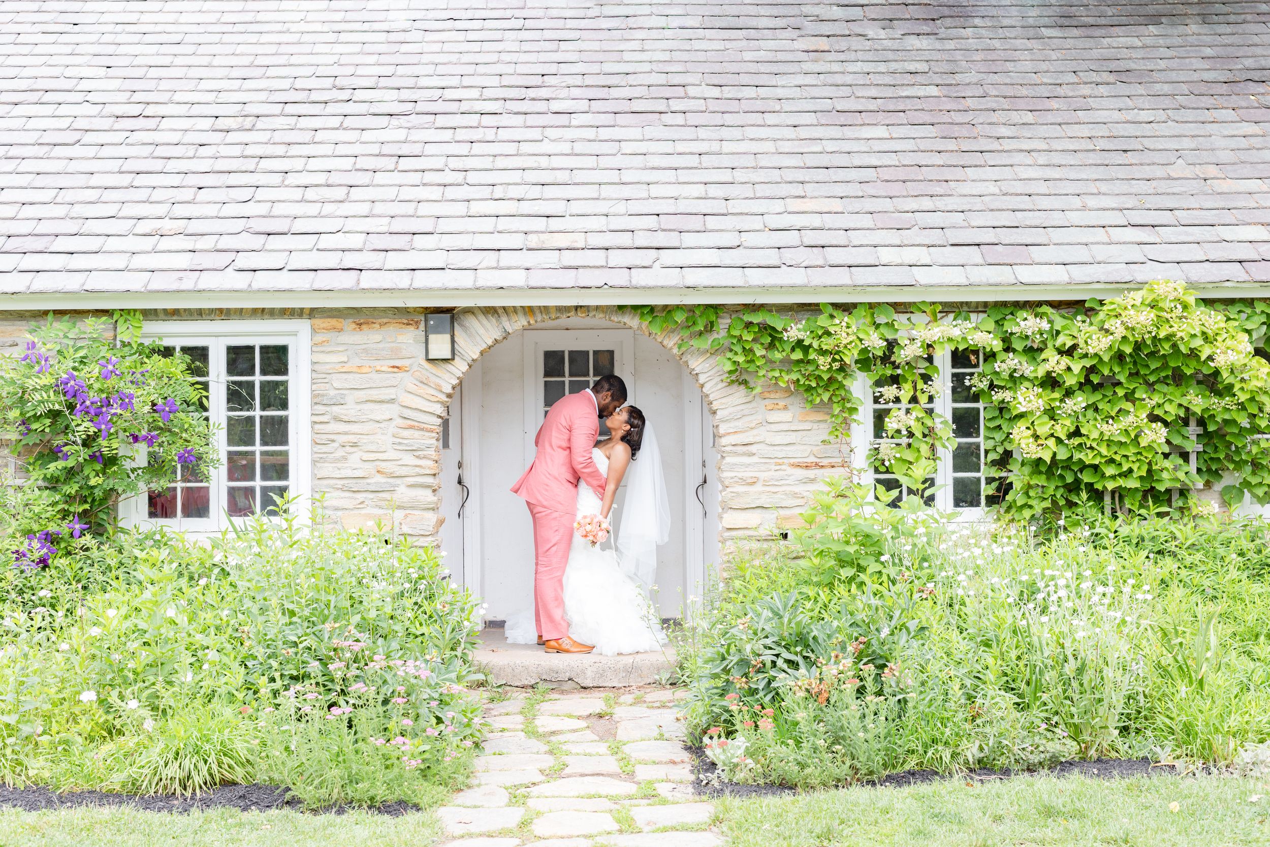 Charming stone cottage with pink door surrounded by blooming garden flowers.