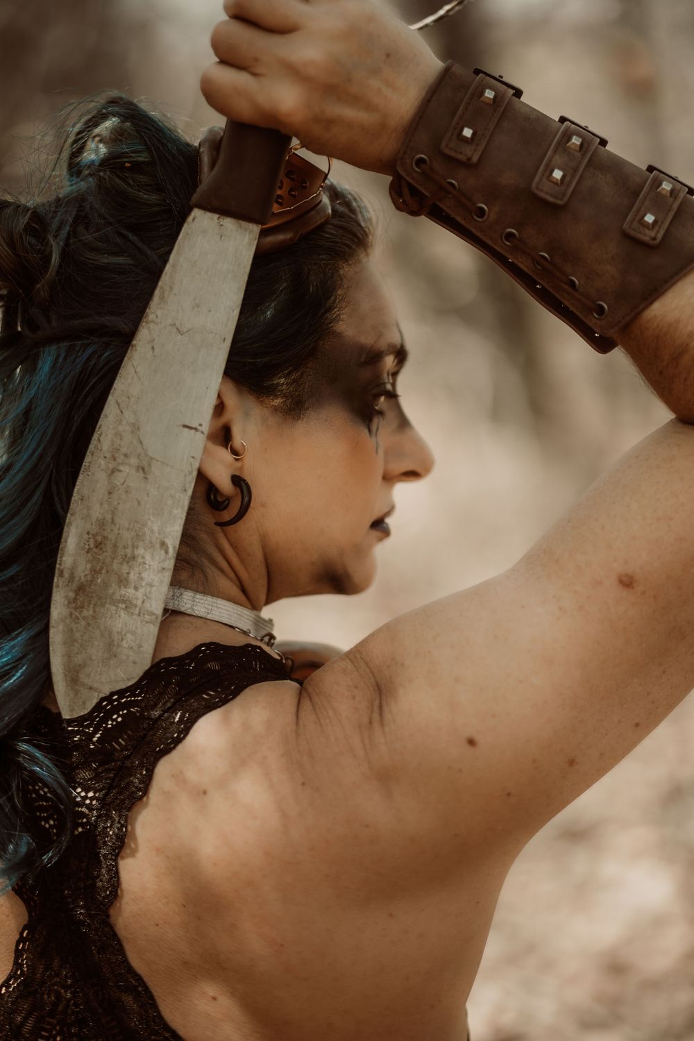 Warrior in leather armor raises sword against dramatic sky in fantasy-inspired action shot.