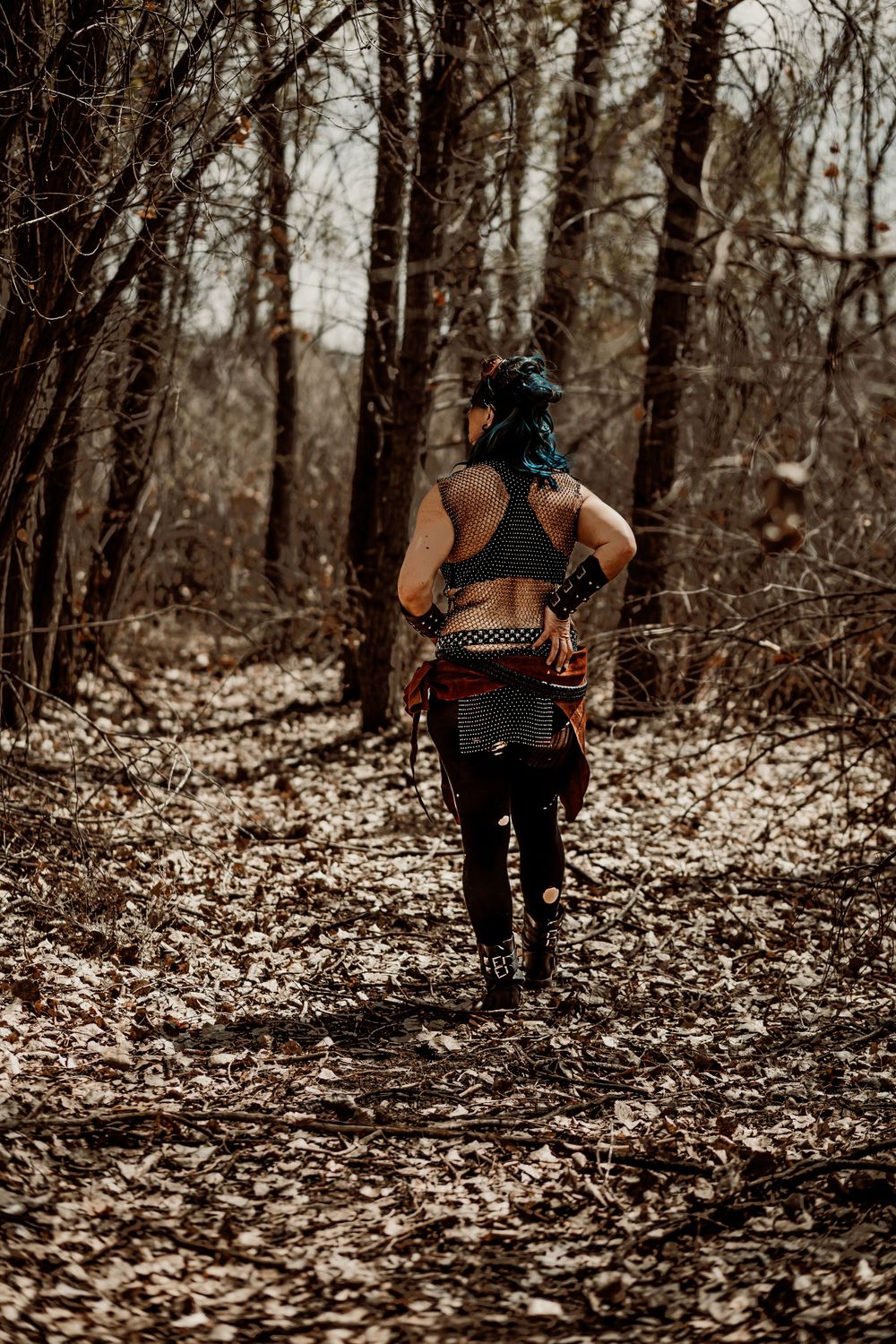 Runner with blue hair traverses autumn forest trail wearing athletic gear.