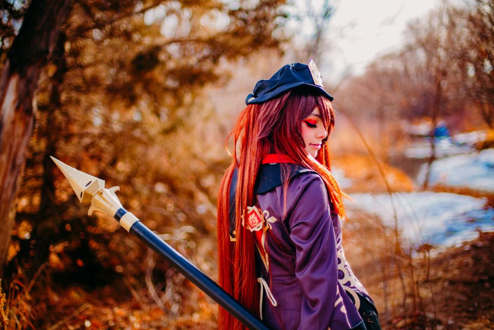 Fantasy cosplay character in purple outfit with red hair against autumn backdrop.