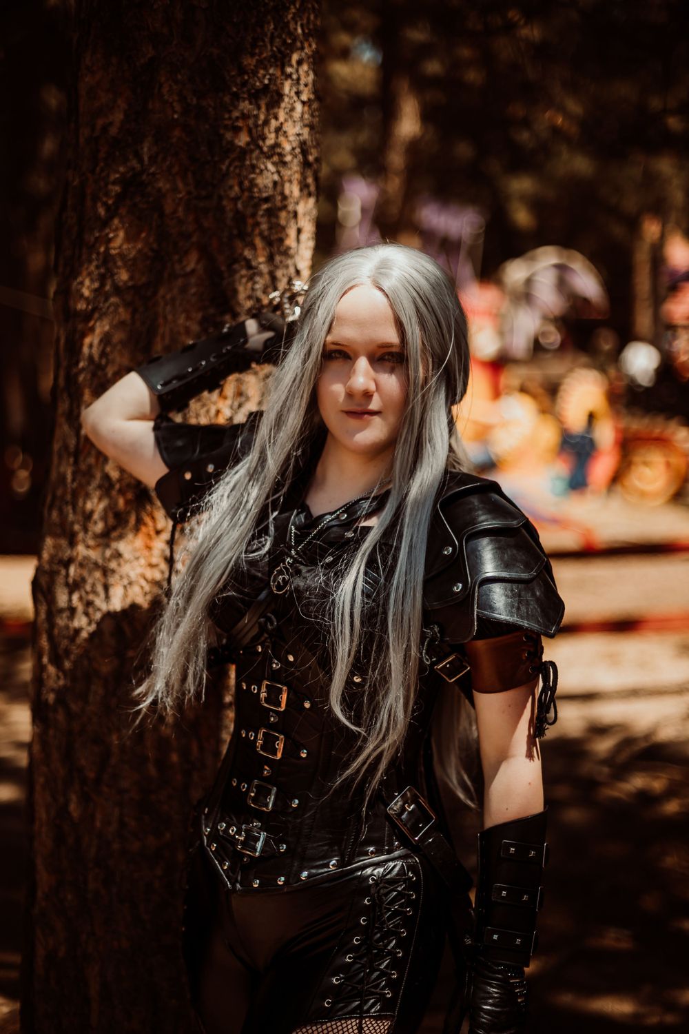Fantasy warrior cosplay featuring silver hair, black leather armor and metal buckles in forest setting.