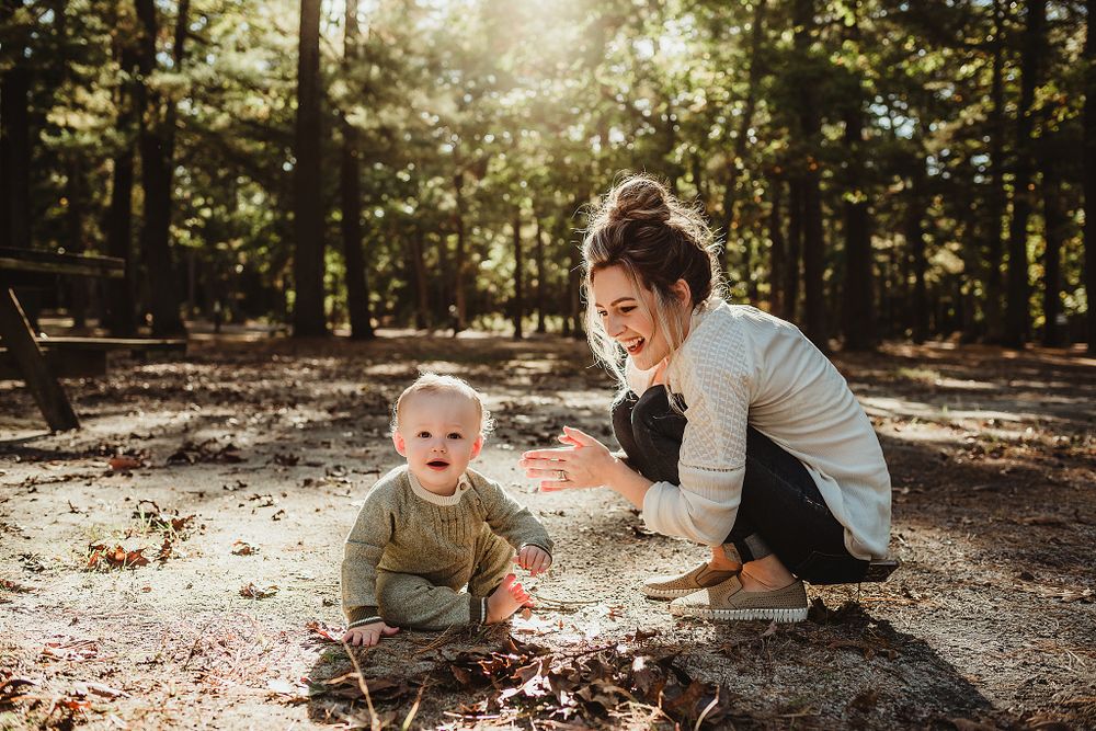 Parent and child explore nature together in a sun-dappled forest setting.
