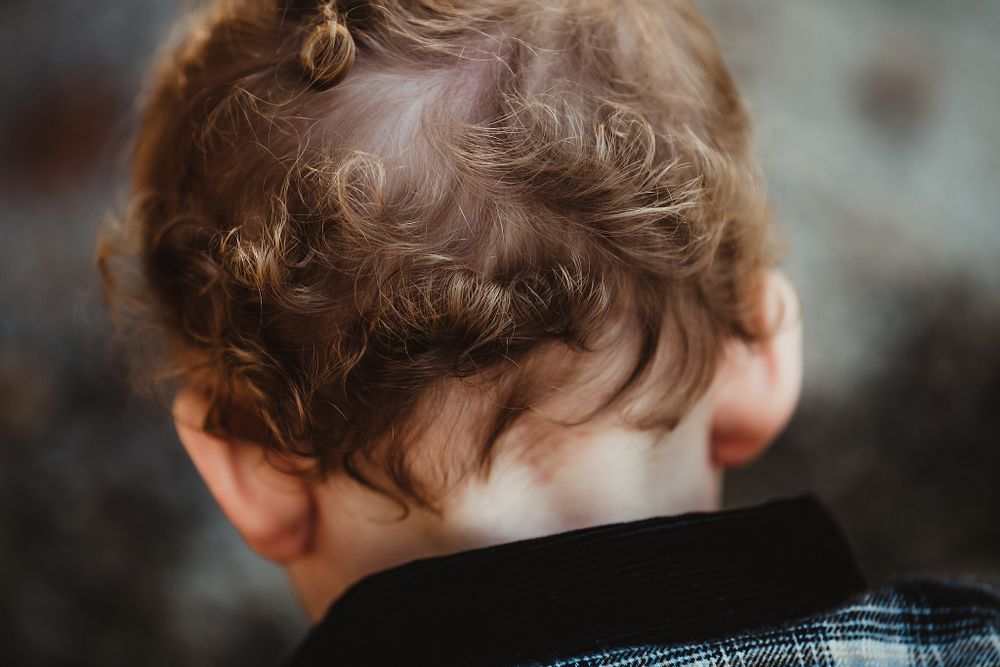 Close-up shot showing curly brown hair from behind against a blurred background.