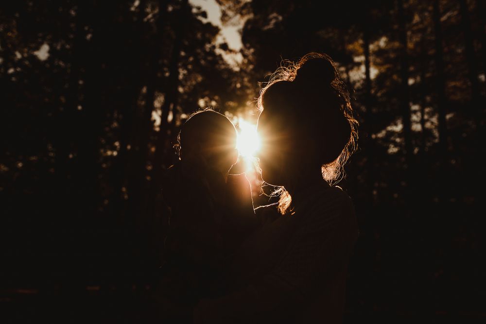 Silhouette against golden sunburst through forest trees.