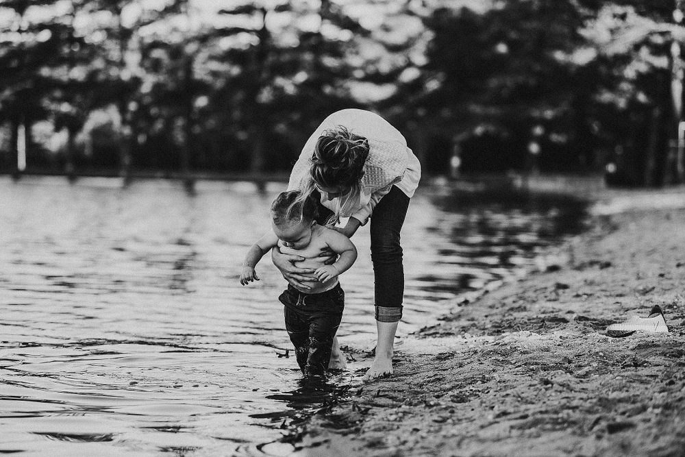 Black and white photo of parent and child playing together in shallow water.