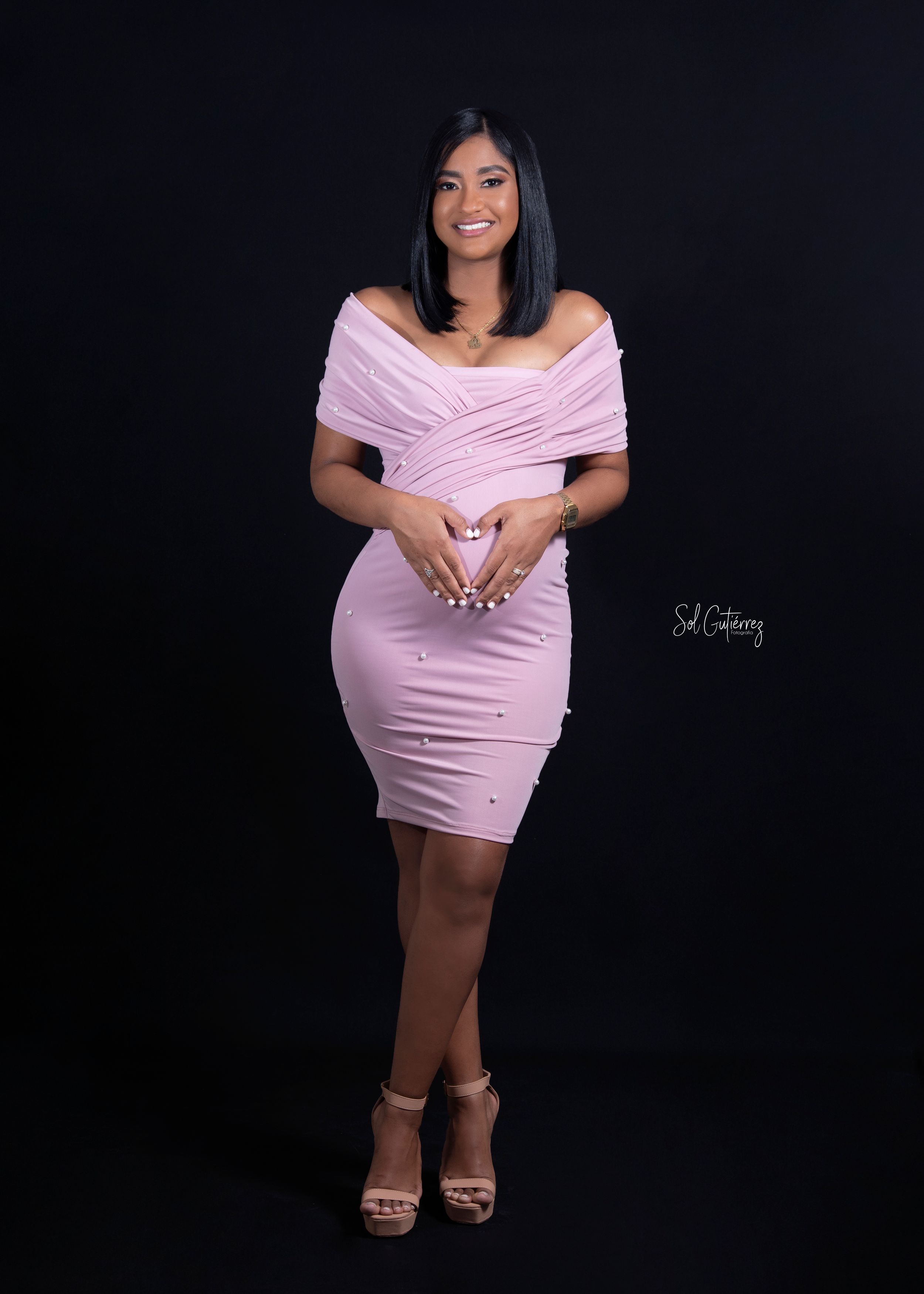 Maternity photoshoot in Allentown PA of pregnant woman in pink dress posing in studio with black background.