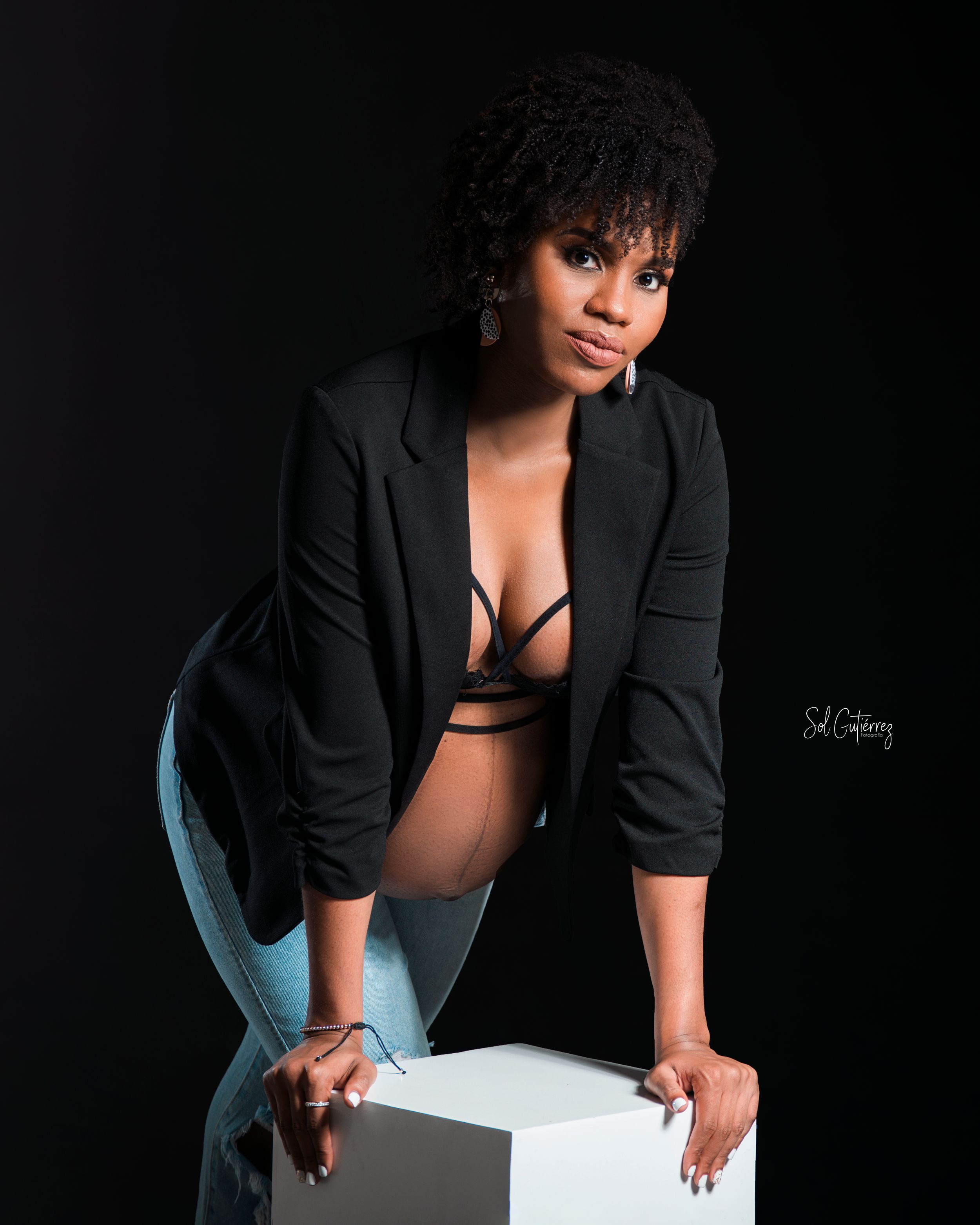 Creative studio portrait in Allentown PA of woman in black blazer posing on cube with dramatic lighting.