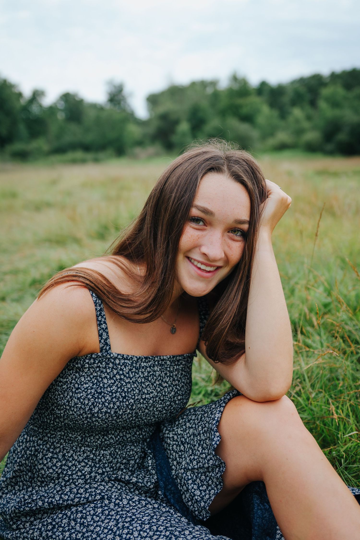 Person in floral dress lounging in green summer field during photoshoot.