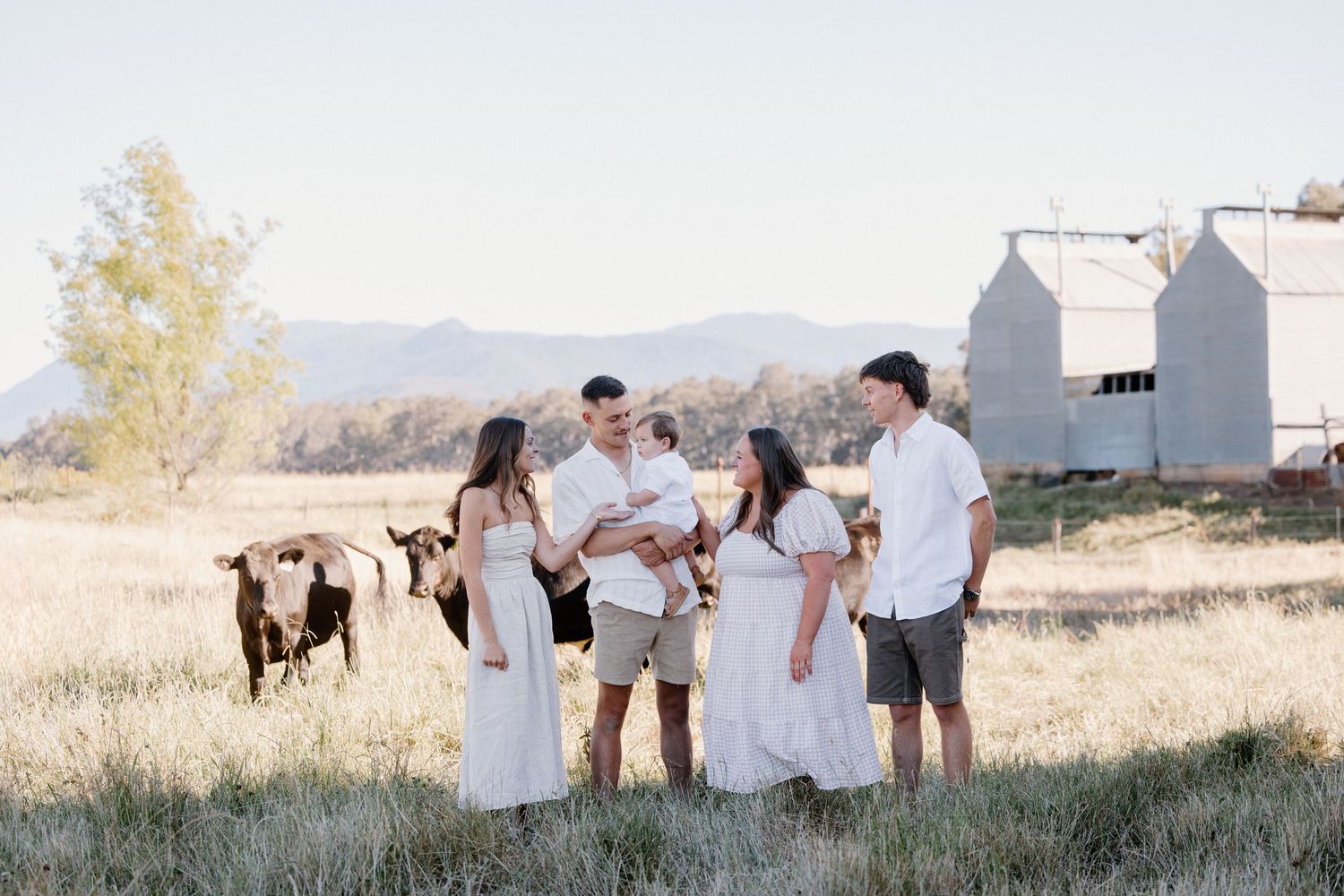 A group in white outfits poses together in a rustic outdoor setting with mountains in the king valley victoria.