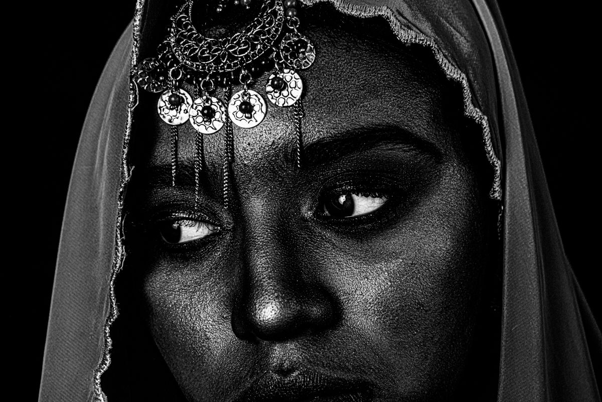 Dramatic black and white portrait with white floral decorations against dark background.