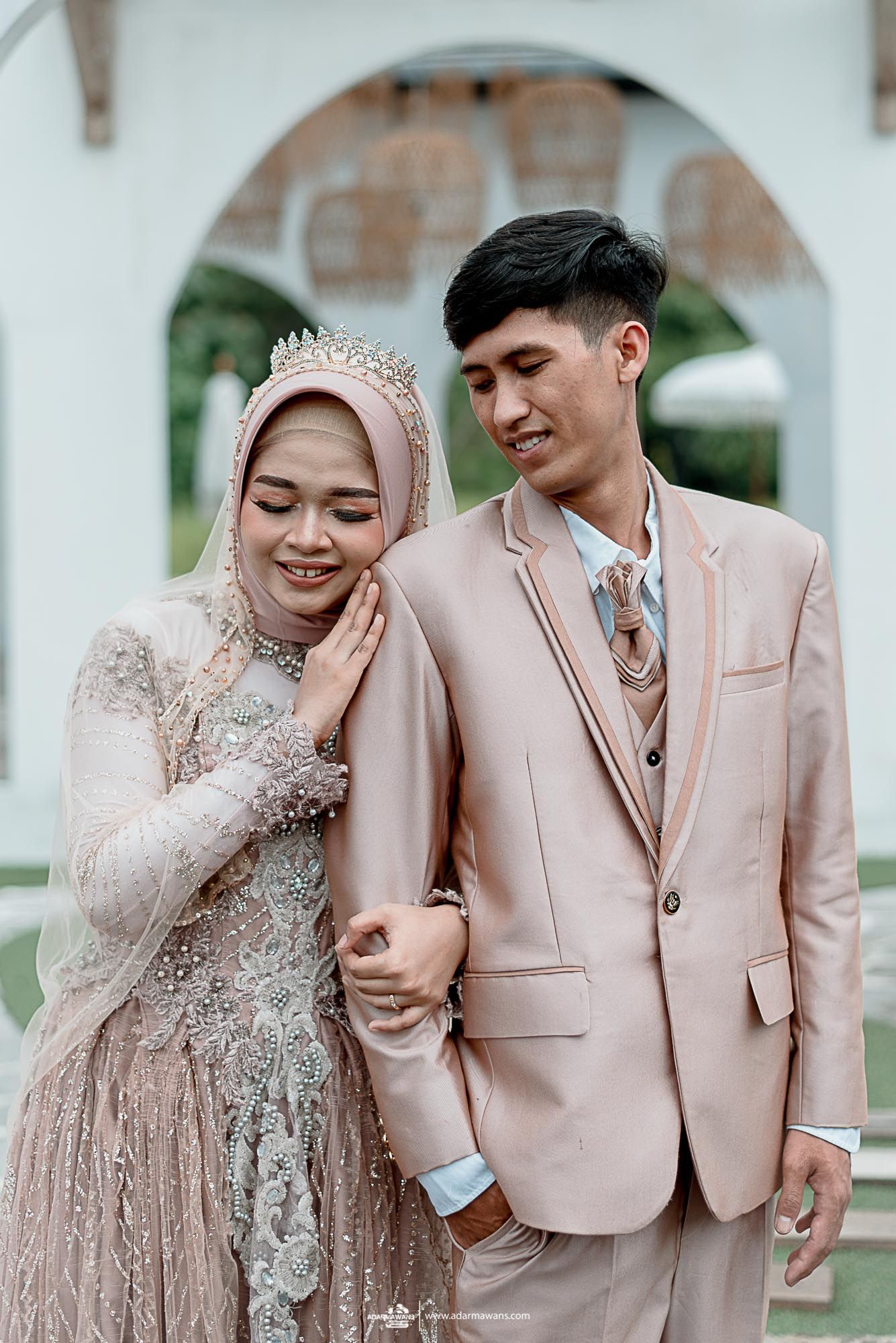 Wedding couple in blush tones posing against white archway background.